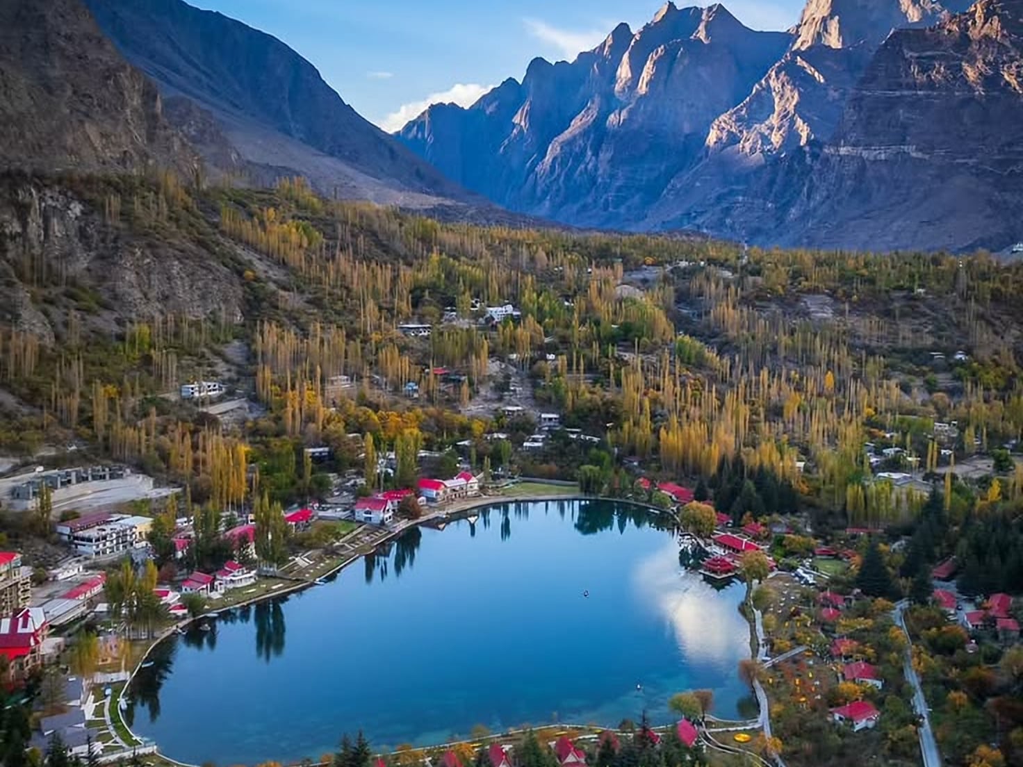 Shangrila Lake (Lower Kachura) near Skardu in autumn from above, ringed by red-roofed buildings and golden poplars below rocky peaks