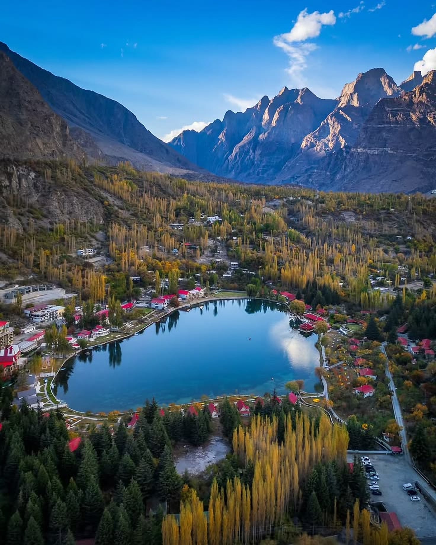 Shangrila Lake (Lower Kachura) near Skardu in autumn from above: a heart-shaped blue lake ringed by red-roofed buildings, golden poplars and rocky peaks