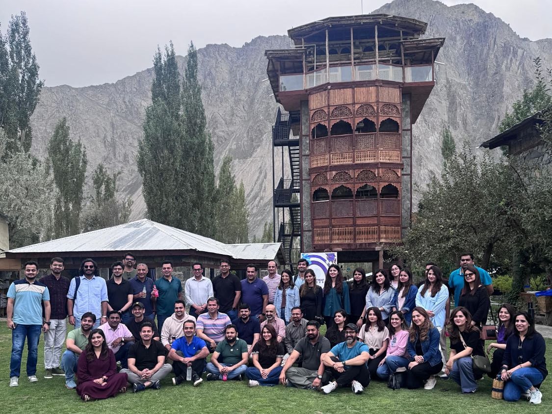 About fifty people from a company retreat posing on the lawn of PC Skardu, in front of its carved wooden tower